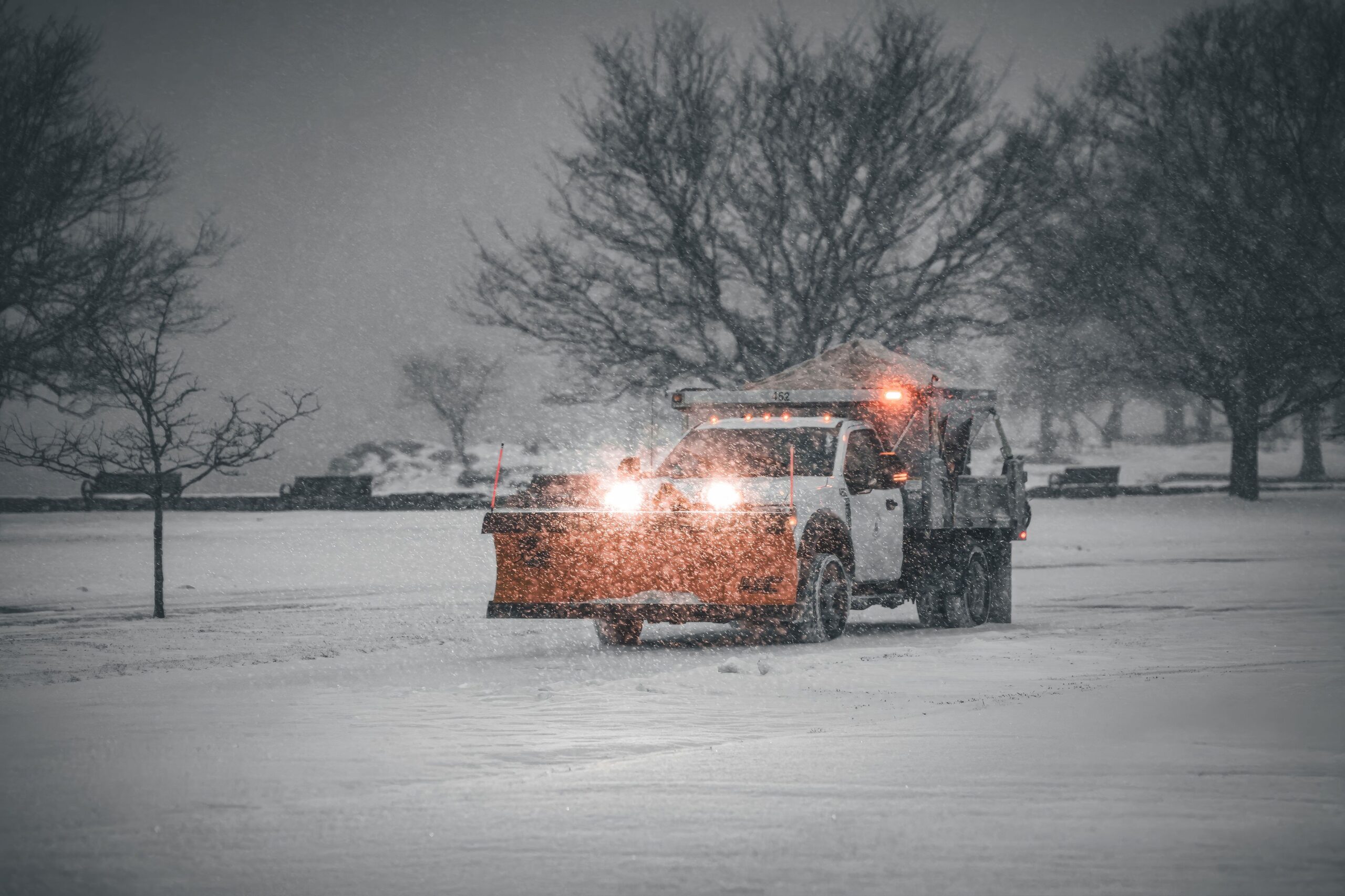A snow plow truck is clearing a snowy road during a winter storm, enhancing road safety.